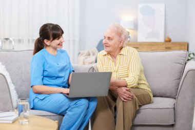 Huzurevinde yaşlı bir kadına dizüstü bilgisayar kullanmayı öğreten bakım işçisi.