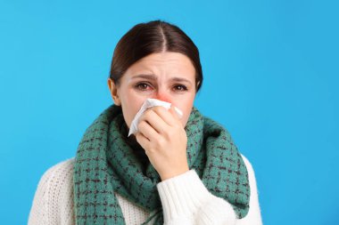 Açık mavi arka planda soğuktan acı çeken, dokuları olan hasta bir kadın. Kırmızı gözler ve burun.