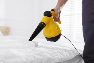 Haşere kontrol işçisi yatağı temizliyor, kapalı alanda buhar temizleyicisiyle, yakın plan