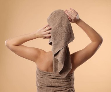 Bej arka planda, havluya sarılı saçları olan kadın.