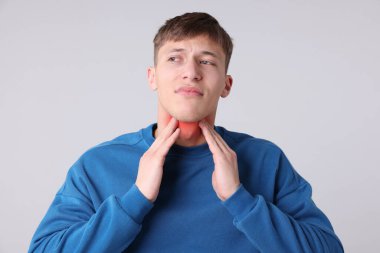 Gri arka planda boğaz ağrısı çeken genç bir adam. Boynunda kırmızı bölge.