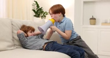 İki kardeş evdeki kanepede megafonla oynaşıyor.