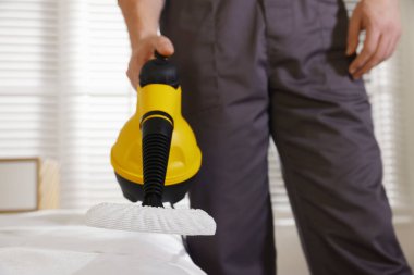 Haşere kontrol işçisi yatağı temizliyor, kapalı alanda buhar temizleyicisiyle, yakın plan