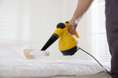 Haşere kontrol işçisi yatağı temizliyor, kapalı alanda buhar temizleyicisiyle, yakın plan
