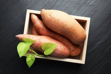 Çiğ patates ve ağaç dalları koyu dokulu masa üzerinde ahşap sandıkta yeşil yapraklar.