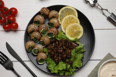 Beyaz ahşap masada servis edilen nefis pişmiş salyangozlar.