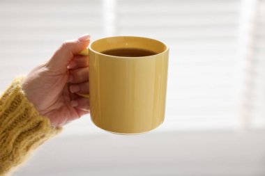 Kapalı mekanda çay içen boş sarı bardağı tutan kadın, yakın plan.