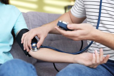 Erkek, kadının kan basıncını evdeki kanepede sphygmomanometre ile ölçüyor.