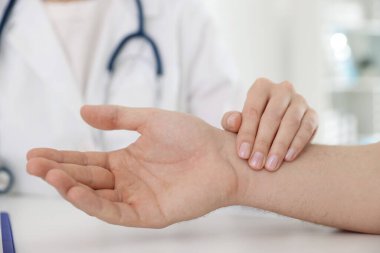 Doktor masadaki parmaklarıyla adamın nabzını kontrol ediyor.