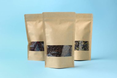 Açık mavi arka planda kahve çekirdekli stand-up çantaları ve çiçek çayı.