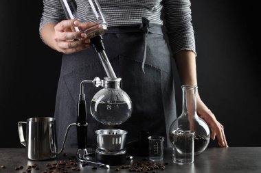 Gri masada vakumlu kahve makinesiyle kahve yapan kadın, yakın plan.