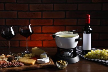 Erimiş peynir, şarap ve ahşap masada atıştırmalıklarla fondü tenceresi (caquelon)