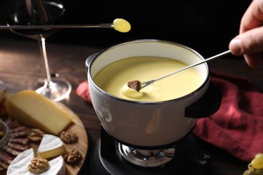 Bir parça ekmek ve üzümü fondü kabına daldıran adam ahşap masada lezzetli erimiş peynirle siyah arka planda atıştırmalıklar, yakın plan