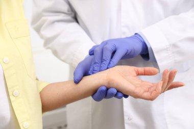 Eldivenli doktor klinikteki hastanın nabzını kontrol ediyor.