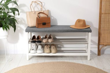 Farklı ayakkabılar, aksesuarlar ve beyaz duvarın yanındaki ev bitkilerinden oluşan ayakkabı deposu.