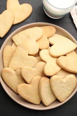 Lezzetli kalp şekilli kurabiyeler ve süt koyu ahşap masa üzerinde, düz yatıyordu.