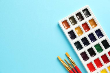 Açık mavi arka planda suluboya palet ve fırçalar, düz. Metin için boşluk