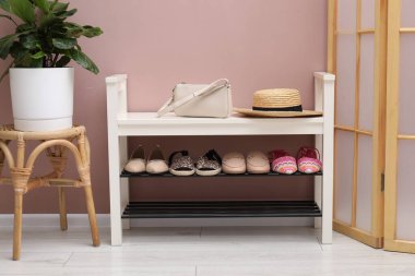 Farklı ayakkabı, aksesuarlar ve kapalı kapılar ardında tozlu pembe duvarın yanında saklama tezgahı.