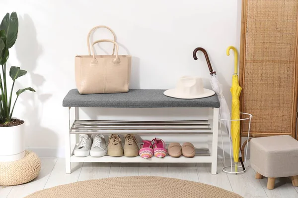 Farklı ayakkabılar, aksesuarlar ve beyaz duvarın yanındaki ev bitkilerinden oluşan ayakkabı deposu.