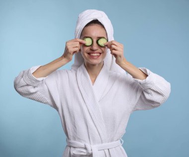 Havluya sarılı güzel bir kadın ve açık mavi arka planda salatalık dilimleri.