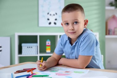 Masada pastel boyayla resim çizen sevimli küçük çocuk.