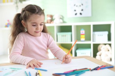 Masada kalemle çizen sevimli küçük kız.