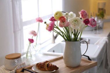 Güzel ranunculus çiçekli ahşap tepsi ve mutfakta taze kruvasan.