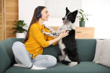 Evdeki kanepede sevimli köpeğiyle kulaklıklı, gülümseyen bir kadın.