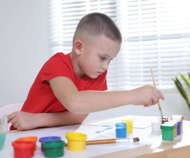 Masada fırçayla resim yapan şirin bir çocuk.
