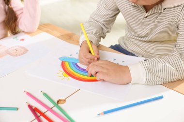 Çocuklar kalemle çizim yapıyor. Kapalı bir masada, yakın plan.