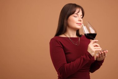 Profesyonel şarap garsonu açık kahverengi arka planda kırmızı şarap tadıyor.