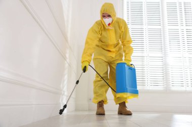 Koruyucu giysiler içinde böcek ilacı sıkan haşere kontrol görevlisi, düşük açılı.