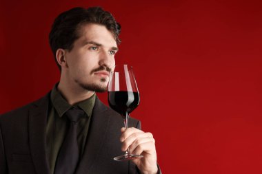 Profesyonel şarap garsonu kırmızı arka planda şarap tadıyor. Metin için boşluk