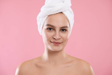 Pembe arka planda havluya sarılı güzel bir kadın.