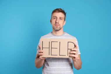 Mutsuz adam elinde kelime yazılı karton tabela açık mavi arka planda yardım