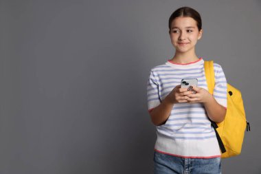 Sırt çantalı genç kız gri arka planda akıllı telefon kullanıyor, mesaj için boşluk