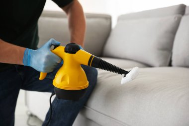 Haşere kontrol işçisi kanepeyi temizliyor. Kapalı alanda buhar temizleyicisi var.