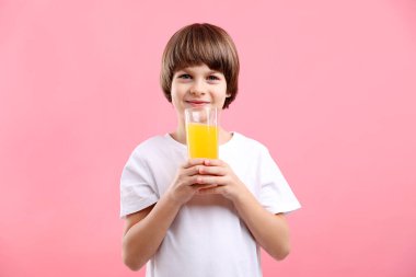 Pembe arka planda bir bardak taze portakal suyu olan çocuk.