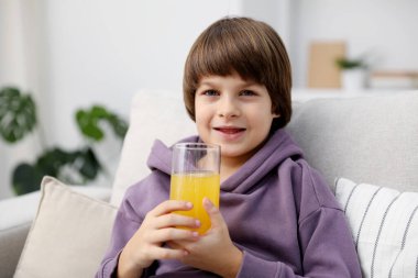 Evdeki kanepede bir bardak taze portakal suyu olan çocuk. Metin için boşluk