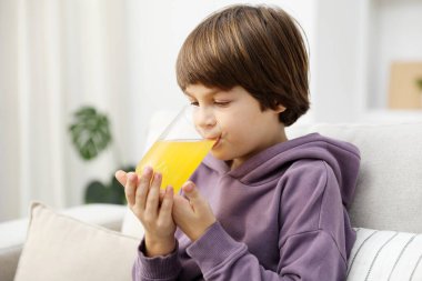 Çocuk evdeki kanepede taze portakal suyu içiyor.