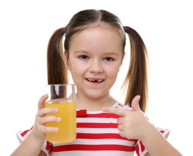 Elinde bir bardak portakal suyu olan küçük kız beyaz arka planda baş parmağını gösteriyor.