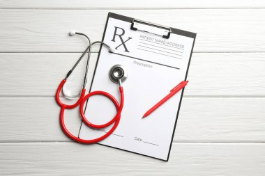 Boş tarlalar, steteskop ve beyaz ahşap masa üzerine düz bir kalem içeren tıbbi reçete formu.
