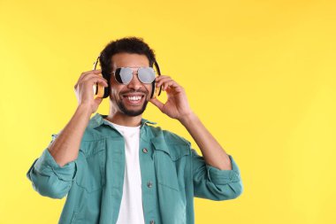 Kulaklıklı adam sarı arka planda müzik dinliyor, mesaj için yer var.