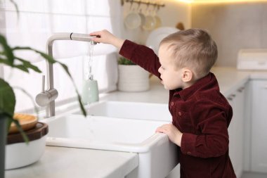 Evde çocuk güvenliği. Küçük çocuk mutfakta lavabo açıyor.