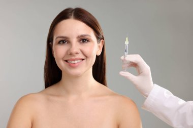 Doktor, gri arka plandaki hastaya yüz enjeksiyonu yapıyor. Yakın plan. Estetik ameliyat