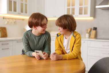 Mutfaktaki ahşap masada akıllı telefonları olan sevimli kardeşler.