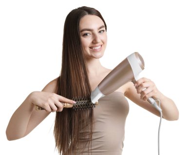 Gülümseyen kadın saçını saç kurutma makinesiyle şekillendiriyor ve beyaz arka planda tarıyor.