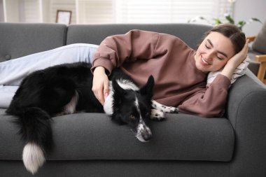 Evdeki kanepede sevimli köpeğiyle gülümseyen kadın.