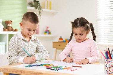 Çocuklar kalem ve pastel boyayla resim çiziyor.