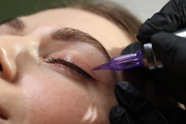 Güzellik uzmanı genç bir kadına kalıcı göz kalemi makyajı yapıyor.